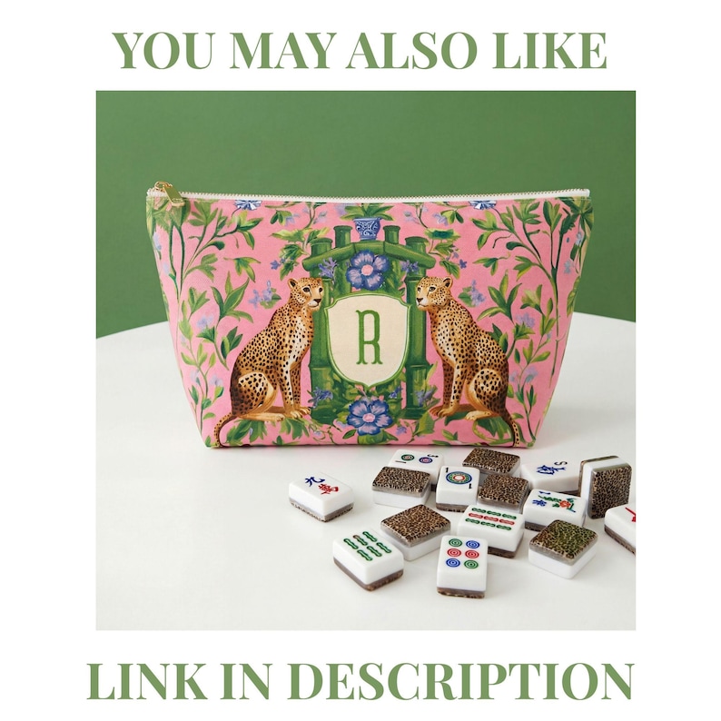 May include: Pink zippered cosmetic bag with a cheetah and floral design, featuring the letter "R" in a green frame. Mahjong tiles are scattered in front of the bag. The text "YOU MAY ALSO LIKE" and "LINK IN DESCRIPTION" are at the top and bottom.