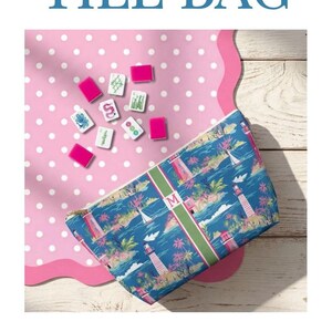 May include: A zippered pouch and a tote bag featuring a blue coastal print with lighthouses, palm trees, and sailboats. Both items have a central green and white vertical stripe with a letter M monogram. Mahjong tiles are shown with the pouch.