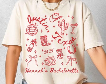 May include: A white t-shirt with a red graphic design that says "Austin, Texas" with various red illustrations including a cactus, cowboy boots, a horseshoe, a disco ball, a margarita glass, a champagne bottle, a bow, and a flower. The text "Hannah's Bachelorette" and the year "2025" are also included in the design.