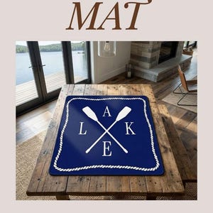 May include: A navy blue Mahjong mat with a white rope border and a crossed oar design. The word "LAKE" is spelled out with the letters L, A, K, and E. The mat is on a wooden surface.