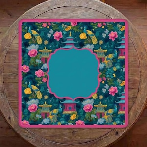 Op de afbeelding: Een vierkante placemat met een donkergroenblauwe achtergrond en een herhalend patroon van gele pauwen, roze pioenrozen en blauwe pagodes. De placemat heeft een effen middenstuk met een geschulpte roze rand en een bijpassende roze buitenrand.