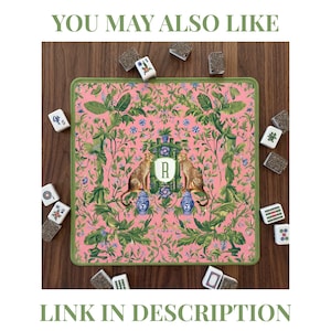May include: A square mahjong mat with a pink background featuring a green botanical pattern, two leopards perched on blue and white vases, and a central shield with the letter R. The mat is surrounded by scattered mahjong tiles.