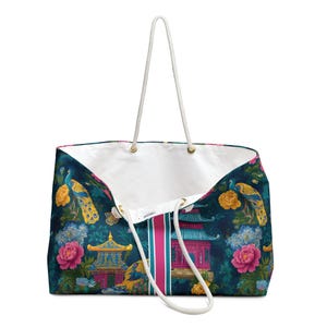 May include: A large tote bag featuring a dark blue background with a repeating pattern of colorful peacocks, pink and yellow flowers, and traditional pagoda structures. The bag has a white interior lining and two white rope handles with gold hardware.