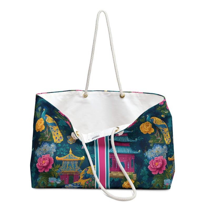 May include: A large tote bag featuring a dark blue background with a repeating pattern of colorful peacocks, pink and yellow flowers, and traditional pagoda structures. The bag has a white interior lining and two white rope handles with gold hardware.