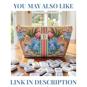 May include: A cosmetic bag with a colorful design featuring a leopard, blue and white vases, and pink flowers. The bag has a gold zipper and the letter "B" on the front. Mahjong tiles are scattered in front of the bag. The text "YOU MAY ALSO LIKE" and "LINK IN DESCRIPTION" are at the top and bottom.