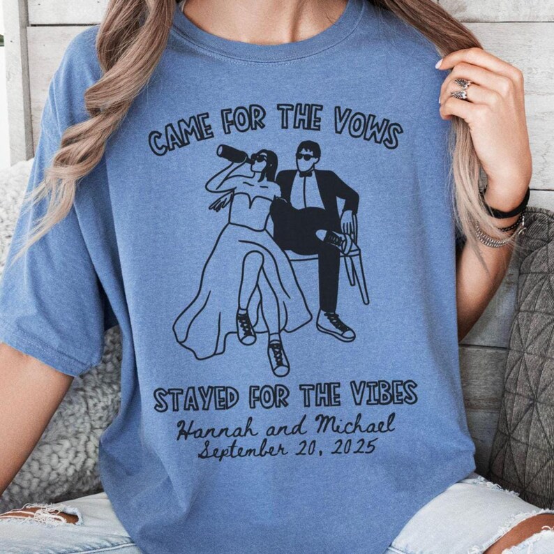 May include: A light blue t-shirt with the text "CAME FOR THE VOWS" and "STAYED FOR THE VIBES". The shirt features a black graphic of a couple, with the names "Hannah and Michael" and the date "September 20, 2025".