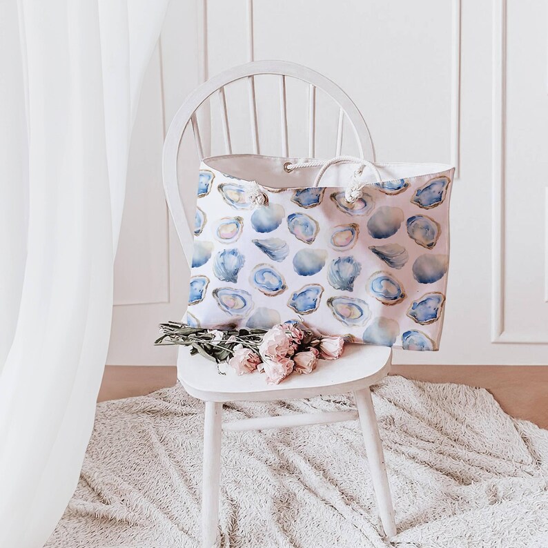 May include: A white tote bag with a blue and white oyster shell pattern sits on a white chair. The bag has a rope handle. A small bouquet of pink roses rests on the chair.