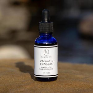 May include: A cobalt blue glass bottle of Vitamin C Oil Serum with a black dropper. The white label features the brand name, product name, and ingredients: Kakadu Plum, CoQ10, and Vitamin C. The bottle contains 1 fl oz of serum.