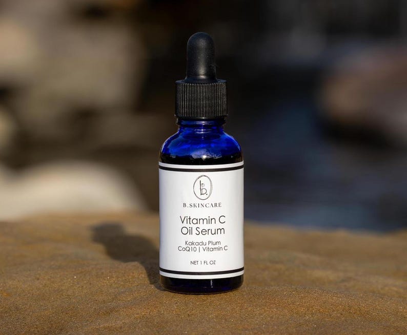 May include: A cobalt blue glass bottle of Vitamin C Oil Serum with a black dropper. The white label features the brand name, product name, and ingredients: Kakadu Plum, CoQ10, and Vitamin C. The bottle contains 1 fl oz of serum.