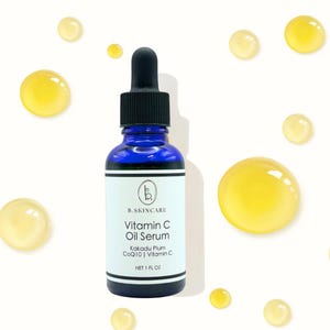 May include: A blue glass bottle of B.SKINCARE Vitamin C Oil Serum with a black dropper. The label includes the product name, ingredients, and brand logo. Yellow oil droplets are scattered around the bottle on a white background. The bottle contains 1 fl oz.