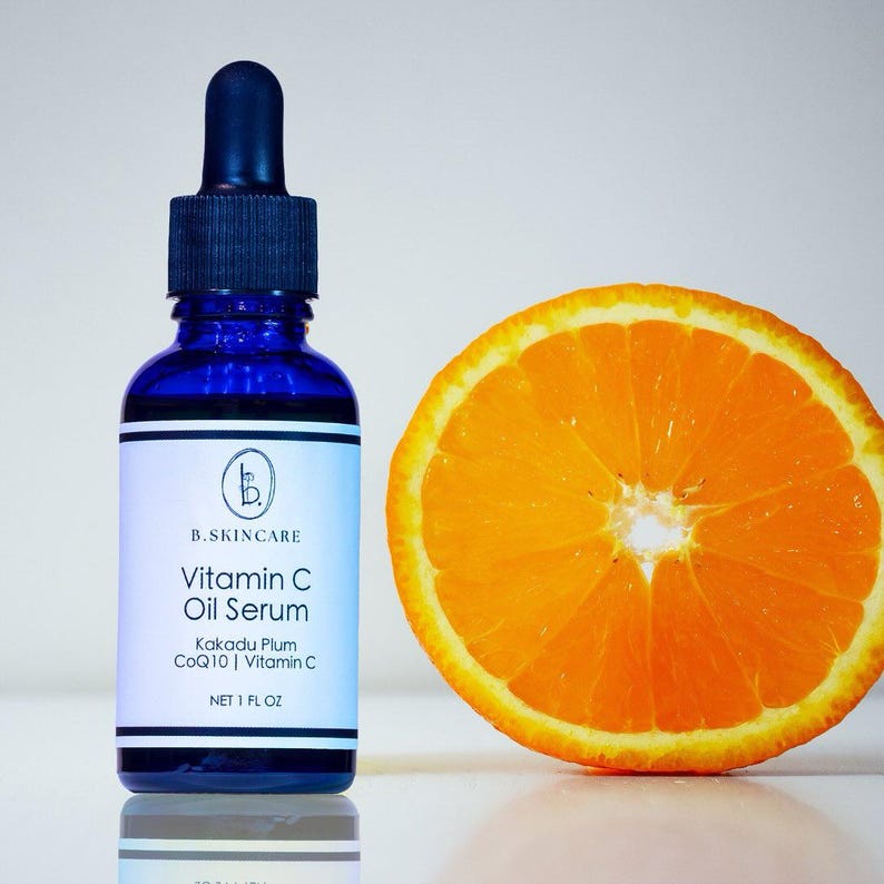 May include: A blue glass bottle of Vitamin C Oil Serum with a dropper, next to a sliced orange. The label reads "B.SKINCARE Vitamin C Oil Serum Kakadu Plum CoQ10 | Vitamin C NET 1 FL OZ". The orange slice is bright orange with a yellow rind.