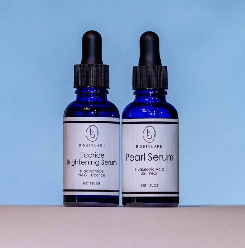 Peut inclure: Deux flacons en verre bleu avec des compte-gouttes contenant des s&eacute;rums pour la peau. Le flacon de gauche est &eacute;tiquet&eacute; "Licorice Brightening Serum" avec les ingr&eacute;dients "Niacinamide NAG | Licorice" et "NET 1 FL OZ". Le flacon de droite est &eacute;tiquet&eacute; "Pearl Serum" avec les ingr&eacute;dients "Hyaluronic Acid B5 | Pearl" et "NET 1 FL OZ".