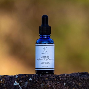 May include: A dark blue glass bottle of B.SKINCARE Licorice Brightening Serum with a black dropper. The white label features the product name and ingredients: Niacinamide, NAG, and Licorice. The bottle contains 1 fl oz of serum.
