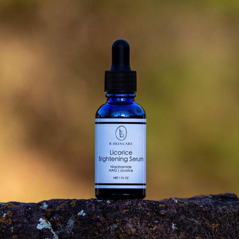 May include: A dark blue glass bottle of B.SKINCARE Licorice Brightening Serum with a black dropper. The white label features the product name and ingredients: Niacinamide, NAG, and Licorice. The bottle contains 1 fl oz of serum.