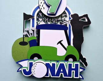 May include: A green golf cart with a golf ball on top, a golfer silhouette, and a green golf course. The number 9 is on a white golf ball with green accents. The name Jonah is written in blue with a white golf ball in the middle.