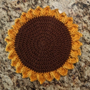 Può includere: Un sottopentola a forma di girasole lavorato a uncinetto, con un centro marrone e petali gialli.