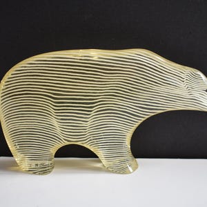 K&ouml;nnte beinhalten: Eine gelbe Glasskulptur eines B&auml;ren mit wei&szlig;en Streifen. Der B&auml;r steht auf allen Vieren und hat ein schlichtes Design.