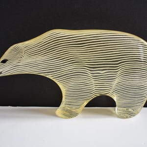 K&ouml;nnte beinhalten: Eine gelbe Glasskulptur eines B&auml;ren mit einem gestreiften Muster. Der B&auml;r steht auf einer wei&szlig;en Oberfl&auml;che.