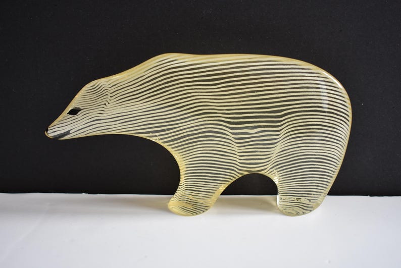 K&ouml;nnte beinhalten: Eine gelbe Glasskulptur eines B&auml;ren mit einem gestreiften Muster. Der B&auml;r steht auf einer wei&szlig;en Oberfl&auml;che.
