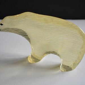 K&ouml;nnte beinhalten: Eine gelbe Glasskulptur eines Eisb&auml;ren mit einem gestreiften Muster. Die Skulptur steht auf einer wei&szlig;en Oberfl&auml;che.