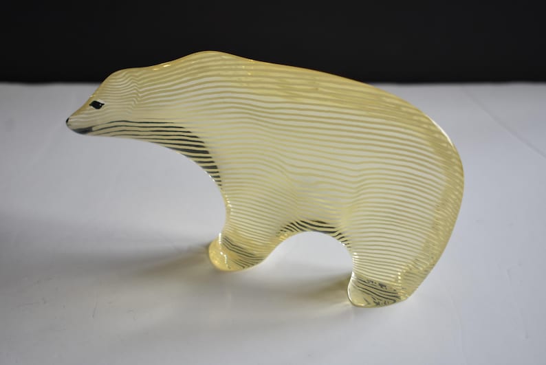 K&ouml;nnte beinhalten: Eine gelbe Glasskulptur eines Eisb&auml;ren mit einem gestreiften Muster. Die Skulptur steht auf einer wei&szlig;en Oberfl&auml;che.