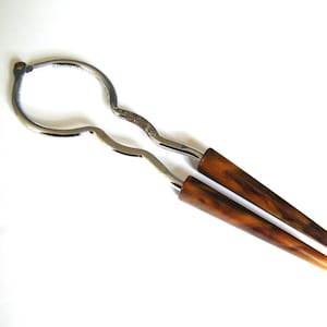 May include: A vintage nutcracker with a silver metal frame and brown, horn-like handles. The nutcracker is open, showing its design. The handles have a marbled appearance.