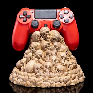 May include: A red video game controller sits atop a pile of small, brown, skull-shaped objects. The controller has a black faceplate and a PlayStation logo.