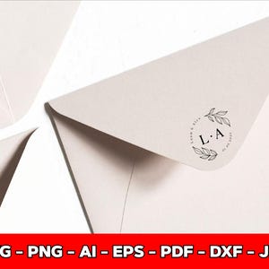 May include: Close-up of several off-white envelopes. One envelope corner features a circular design with the initials "L.A." and the date "01.01.2023" inside a wreath of leaves. The image is set against a white background.