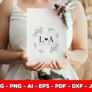 May include: A cream-colored wedding invitation featuring a black floral wreath design with the initials "L&hearts;A" and the date "01.05.2025". The invitation is held by a person wearing a white dress. The bottom of the image has the text "SVG - PNG - AI - EPS - PDF - DXF - JPG".