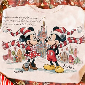 Peut inclure: Un sweat-shirt crème avec une illustration de Mickey et Minnie Mouse en tenues d'hiver, devant un château. Le texte dit "Together under the Christmas magic..." avec les noms "Minnie" et "Mickey". Les personnages portent des écharpes et bonnets rayés.