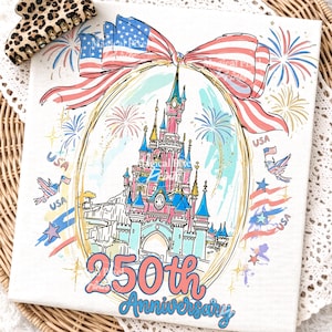 May include: A white canvas print featuring a pink and blue castle design within a gold oval, adorned with an American flag bow and fireworks. The text "250th Anniversary" is displayed in pink and blue. A leopard print hair clip is in the upper left corner.