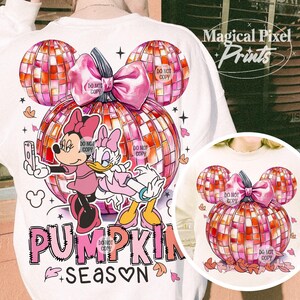 K&ouml;nnte beinhalten: Ein wei&szlig;es Sweatshirt mit einem pinkfarbenen und orangenen K&uuml;rbisdesign. Der K&uuml;rbis besteht aus einer Discokugel und hat eine rosafarbene Schleife oben drauf. Mickey Mouse und Daisy Duck stehen vor dem K&uuml;rbis. Der Text "Pumpkin Season" steht unter dem K&uuml;rbis.