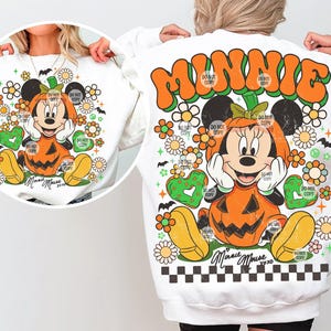 May include: White sweatshirt featuring a Minnie Mouse design in a pumpkin costume. The design includes orange, yellow, green, and black elements, with floral and heart accents. The text "MINNIE" and "Minnie Mouse xoxo" are also visible.