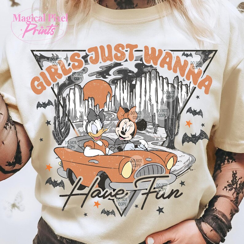 May include: A white t-shirt with a vintage-style graphic featuring two cartoon characters driving a red car. The text "Girls Just Wanna Have Fun" is written in a retro font.