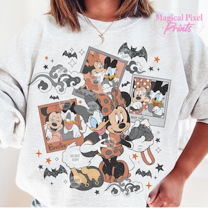 Op de afbeelding: Een wit sweatshirt met een grafische print van Mickey Mouse en Minnie Mouse gekleed in Halloween-kostuums. De print heeft een vintage fotocollage-stijl met de tekst "Girls just wanna have fun" en "Best Friends" in een zwart-oranje kleurenschema.