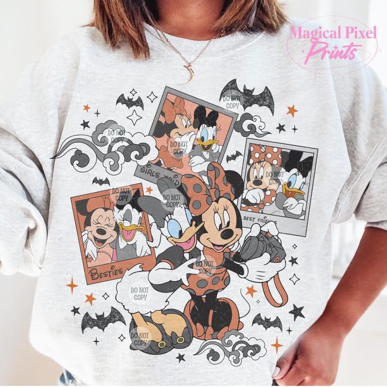 Op de afbeelding: Een wit sweatshirt met een grafische print van Mickey Mouse en Minnie Mouse gekleed in Halloween-kostuums. De print heeft een vintage fotocollage-stijl met de tekst "Girls just wanna have fun" en "Best Friends" in een zwart-oranje kleurenschema.
