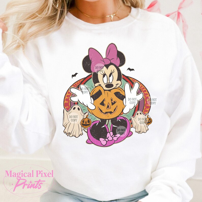 May include: White sweatshirt with a Halloween Minnie Mouse design. Minnie Mouse is holding a jack-o'-lantern, with ghosts and bats. The design includes the text "DO NOT COPY" and "Magical Pixel Prints".