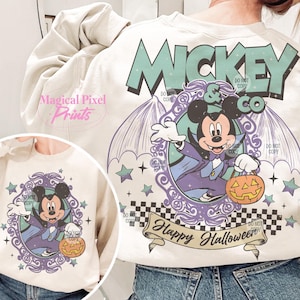 Puede incluir: Una sudadera blanca con un gr&aacute;fico morado y verde de Mickey Mouse vestido de vampiro sosteniendo una calabaza de Halloween. El gr&aacute;fico dice "Mickey & Co" y "Feliz Halloween".