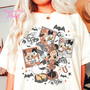 Op de afbeelding: Een wit T-shirt met een grafische print van Mickey Mouse en Minnie Mouse verkleed als heksen. De grafiek bevat de tekst "Girls just wanna have fun" en "Best friends".