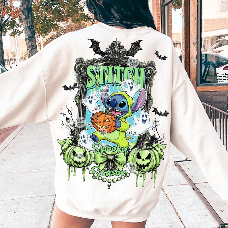 May include: Cream-colored sweatshirt featuring a Halloween-themed graphic. The design includes the word "Stitch" above a cartoon character holding a pumpkin, surrounded by ghosts and pumpkins. The phrase "Spooky Season" is also present.