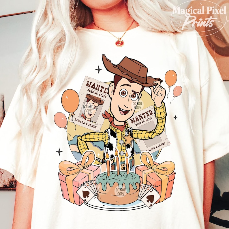 May include: A white t-shirt with a cartoon image of Woody from Toy Story. Woody is wearing his signature cowboy hat and vest. He is holding a wanted poster and standing in front of a birthday cake with candles. The text on the wanted posters reads "WANTED DEAD OR ALIVE".