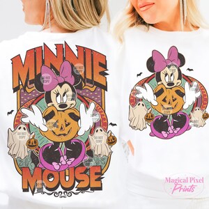 May include: White long-sleeve shirt with a Halloween Minnie Mouse design. The design features Minnie Mouse, a jack-o'-lantern, ghosts, and the words "MINNIE MOUSE" in orange and brown. The shirt has a retro, vintage style.