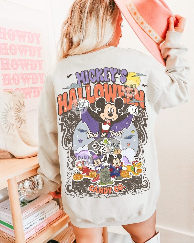 Może przedstawiać: Jasnoszara bluza z kolorową grafiką Halloween. Projekt przedstawia Myszka Miki przebranego za wampira, z napisami "Mickey's Halloween" i "Trick or Treat". Bluza ma r&oacute;wnież logo "Candy Co.".