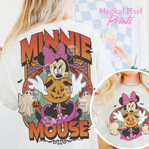 May include: Cream-coloured t-shirt with a Halloween-themed Minnie Mouse design. The graphic shows Minnie Mouse with a purple bow, holding a jack-o'-lantern, and surrounded by ghosts and bats. The word "MINNIE" is at the top, and "MOUSE" is at the bottom.