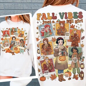 May include: White sweatshirt with a colorful graphic featuring cartoon images of princesses in fall attire. The text "FALL VIBES just a fall girl" is printed on the back. The design includes pumpkins, leaves, and the words "DO NOT COPY".