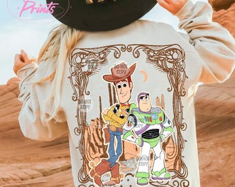 May include: A light beige sweatshirt with a vintage-style graphic print of Woody and Buzz Lightyear from Toy Story. The graphic features a brown frame with a western-themed design and the text "You got a friend in me".