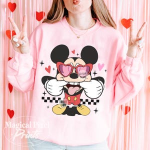 Pu&ograve; includere: Felpa rosa con una grafica di Topolino che indossa occhiali a forma di cuore e un motivo a scacchi. Il testo "Do Not Copy" &egrave; visibile sulla grafica.