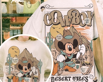 May include: A beige sweatshirt with a vintage-style graphic featuring Mickey Mouse dressed as a cowboy with the text "COWBOY" and "DESERT VIBES ON MY MIND".