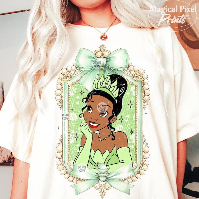 May include: A white t-shirt with a green and gold frame featuring a cartoon image of Princess Tiana from Disney's The Princess and the Frog. The frame is decorated with pearls and a green bow. The text "DO NOT COPY" appears multiple times on the image.