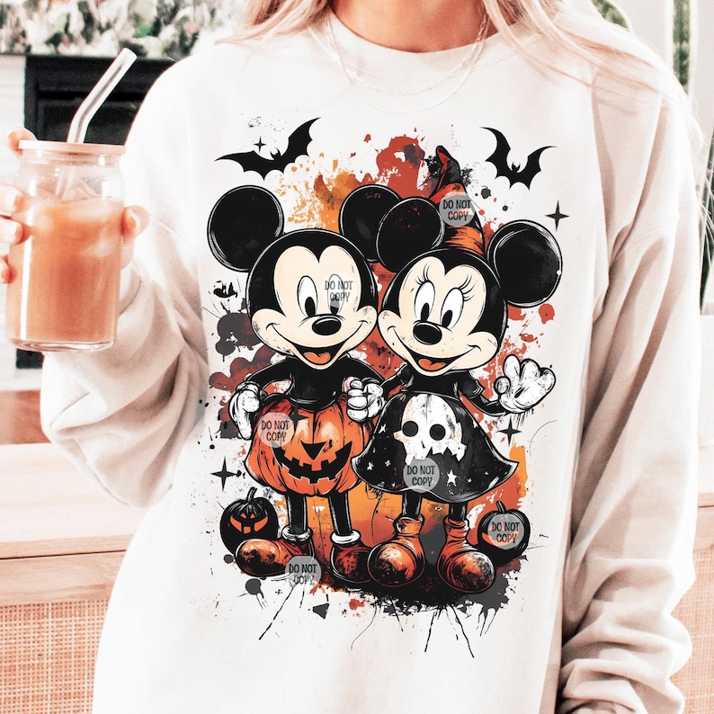 May include: White sweatshirt featuring Mickey and Minnie Mouse in Halloween costumes. Mickey wears a pumpkin outfit, and Minnie wears a witch hat and skull dress. The design includes bats and the text "DO NOT COPY".
